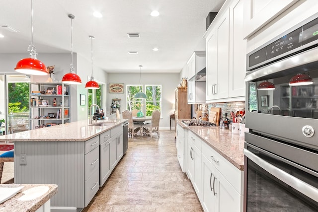 kitchen featuring sink, decorative light fixtures, a kitchen island with sink, white cabinets, and appliances with stainless steel finishes