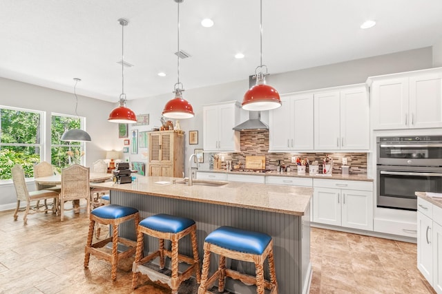 kitchen with white cabinets, sink, hanging light fixtures, and an island with sink