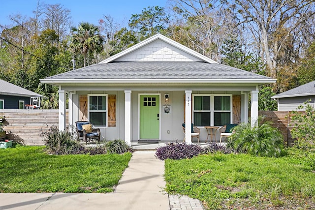 bungalow-style home with a front yard, a porch, fence, and roof with shingles