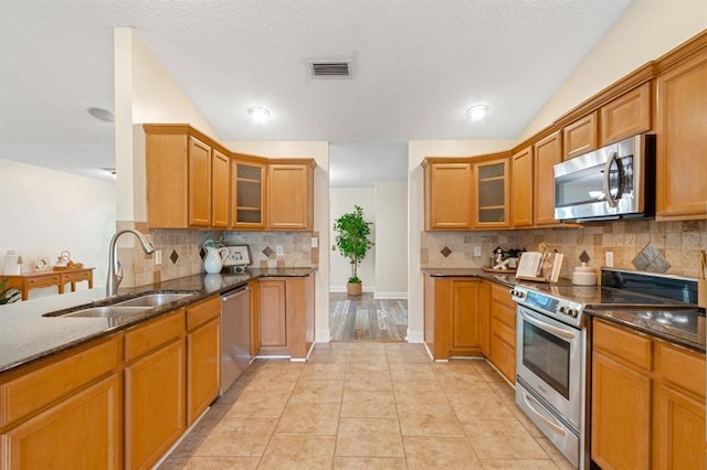 kitchen featuring sink, vaulted ceiling, dark stone counters, and appliances with stainless steel finishes