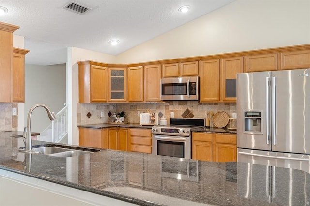 kitchen featuring vaulted ceiling, sink, backsplash, dark stone counters, and stainless steel appliances