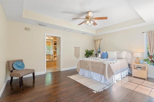 bedroom featuring ceiling fan, wood-type flooring, a tray ceiling, and connected bathroom