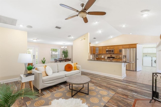 living room with vaulted ceiling, dark hardwood / wood-style floors, ceiling fan with notable chandelier, and washing machine and clothes dryer