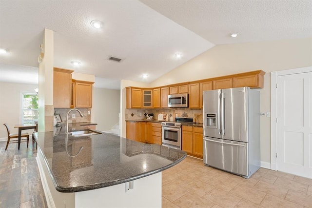 kitchen with sink, kitchen peninsula, dark stone counters, and appliances with stainless steel finishes