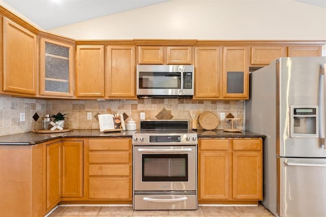 kitchen with tasteful backsplash, vaulted ceiling, light tile patterned floors, appliances with stainless steel finishes, and dark stone counters