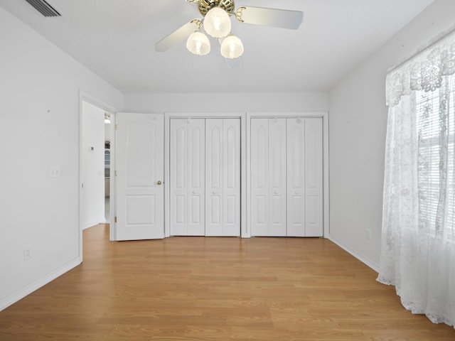 unfurnished bedroom featuring ceiling fan, multiple closets, and light wood-type flooring