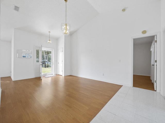 spare room featuring high vaulted ceiling, light hardwood / wood-style floors, and a chandelier