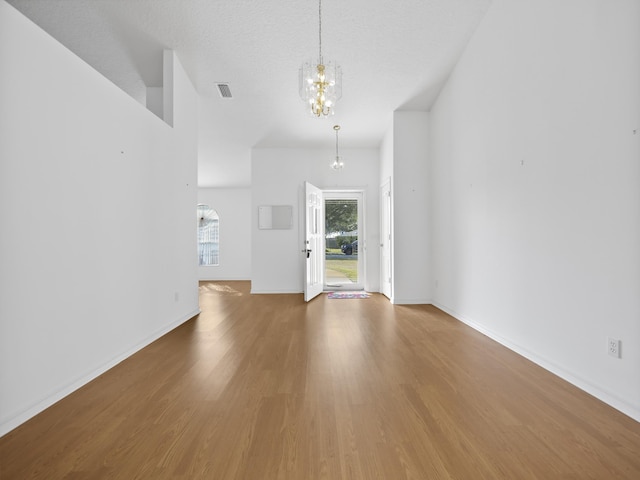 unfurnished living room featuring hardwood / wood-style floors, a textured ceiling, and an inviting chandelier