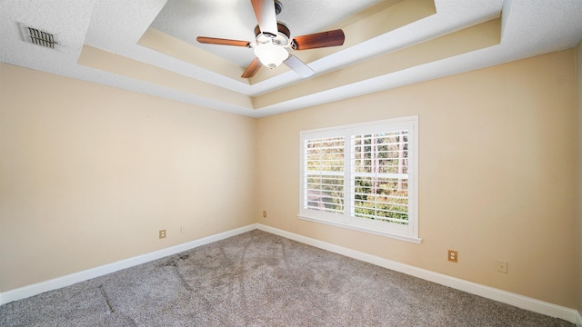 empty room featuring carpet flooring, ceiling fan, and a raised ceiling