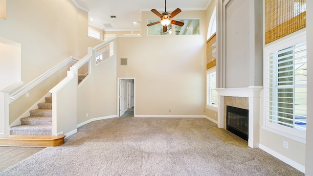 unfurnished living room with a tiled fireplace, ceiling fan, and a towering ceiling