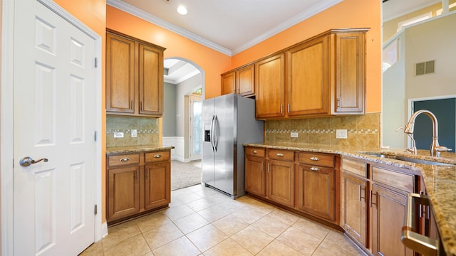 kitchen with stainless steel fridge, light tile patterned floors, light stone counters, and sink