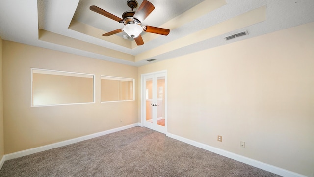 carpeted empty room with a raised ceiling and ceiling fan