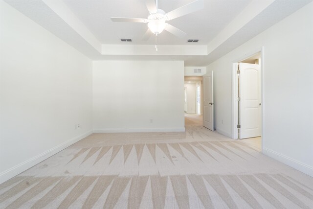 spare room with ceiling fan, light colored carpet, and a raised ceiling