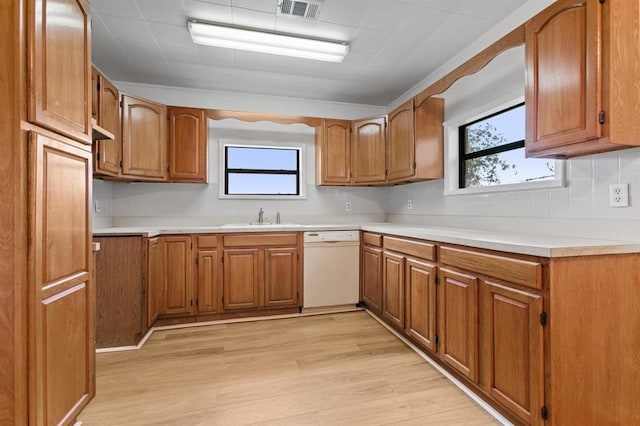 kitchen with white dishwasher, a sink, light wood-style floors, brown cabinetry, and visible vents
