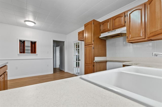 kitchen with brown cabinetry, decorative backsplash, wood finished floors, light countertops, and under cabinet range hood
