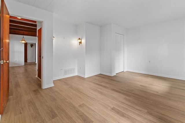 spare room with baseboards, beamed ceiling, light wood-style flooring, and visible vents