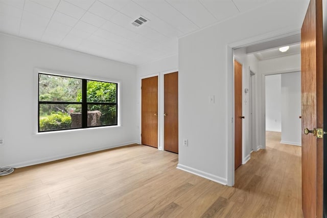 unfurnished bedroom featuring visible vents, baseboards, multiple closets, and light wood-type flooring