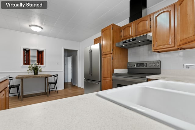 kitchen with appliances with stainless steel finishes, tasteful backsplash, light countertops, light wood-type flooring, and under cabinet range hood