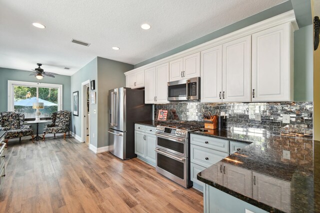 kitchen featuring white cabinetry, ceiling fan, dark stone countertops, light hardwood / wood-style floors, and appliances with stainless steel finishes