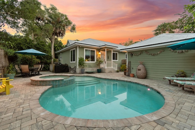 back house at dusk with a patio area and a pool with hot tub