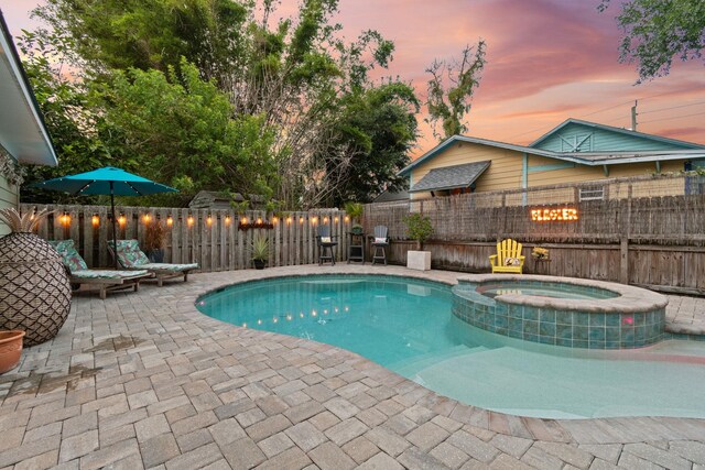 pool at dusk featuring a patio area and an in ground hot tub