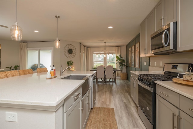 kitchen with stainless steel appliances, gray cabinets, a kitchen island with sink, and hanging light fixtures