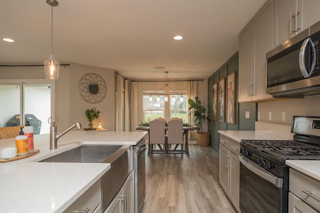 kitchen with gray cabinets, decorative light fixtures, hardwood / wood-style flooring, light stone counters, and stainless steel appliances