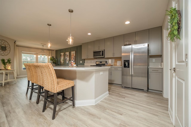 kitchen with pendant lighting, light hardwood / wood-style flooring, gray cabinetry, stainless steel appliances, and a kitchen island