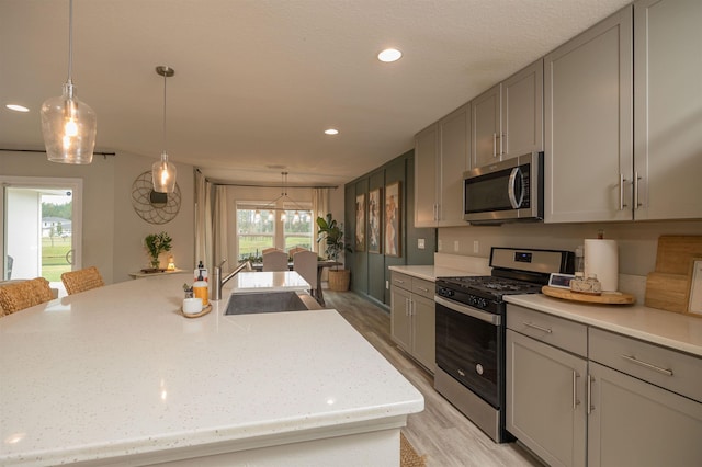 kitchen featuring stainless steel appliances, sink, pendant lighting, and a kitchen island with sink