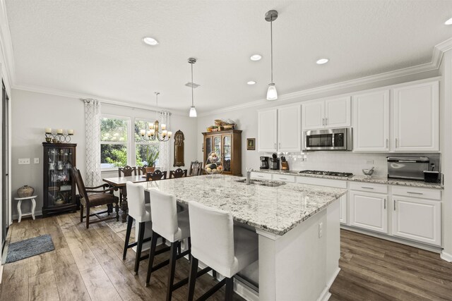 kitchen with a notable chandelier, a sink, stainless steel appliances, white cabinetry, and ornamental molding