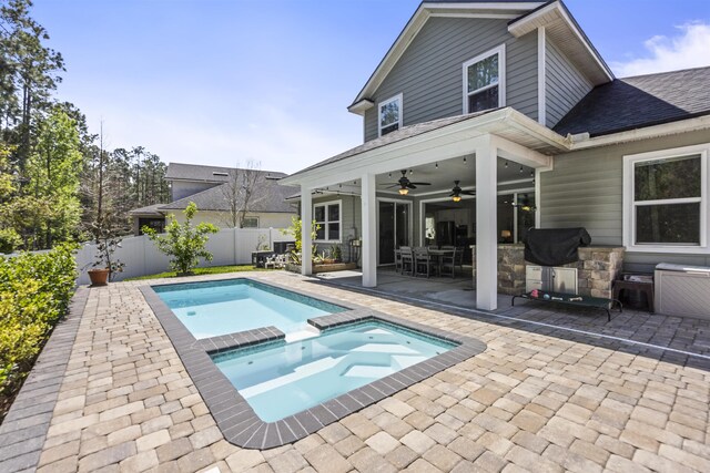 rear view of house featuring a ceiling fan, a pool with connected hot tub, fence, a patio, and a shingled roof