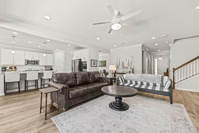 living area featuring light wood-type flooring, a ceiling fan, stairs, and a textured ceiling
