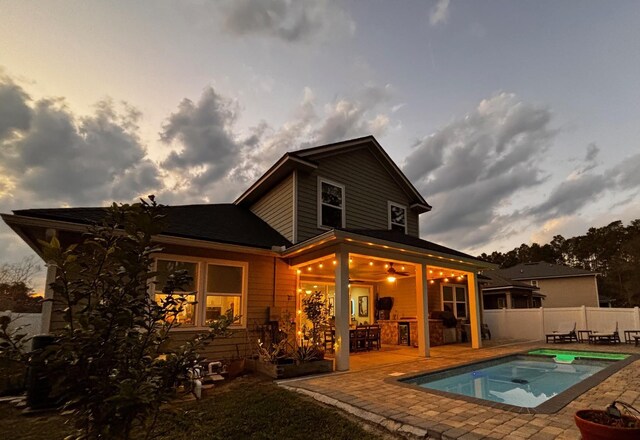 back of property at dusk with fence, a jacuzzi, and a patio area