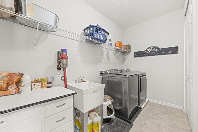 clothes washing area featuring washing machine and clothes dryer, laundry area, a sink, a textured ceiling, and baseboards