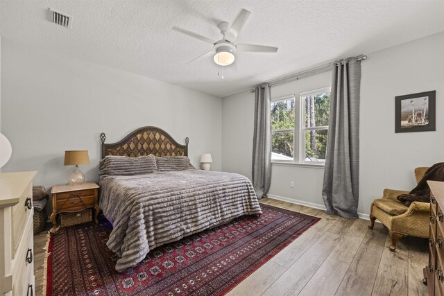 bedroom with a textured ceiling, visible vents, ceiling fan, and light wood finished floors