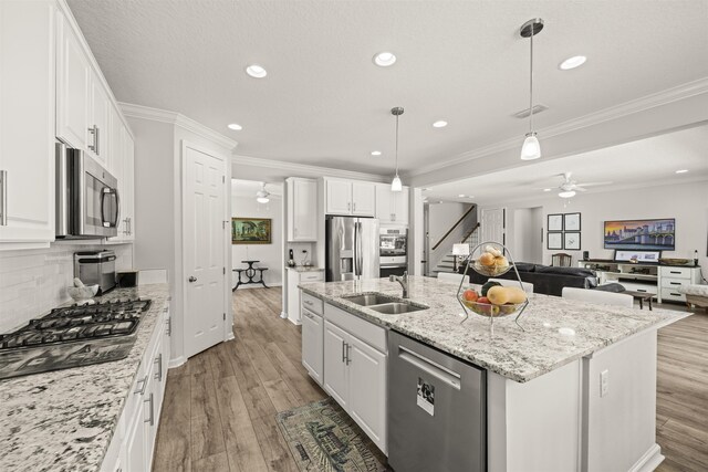 kitchen featuring appliances with stainless steel finishes, a sink, light wood finished floors, an island with sink, and a ceiling fan