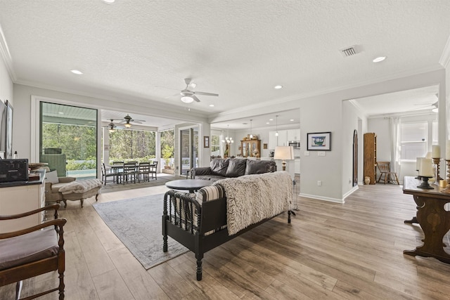 living area with a ceiling fan, a textured ceiling, visible vents, crown molding, and light wood-type flooring