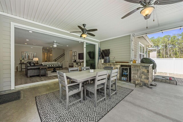 view of patio featuring fence, a sink, an outdoor kitchen, outdoor dining area, and a ceiling fan