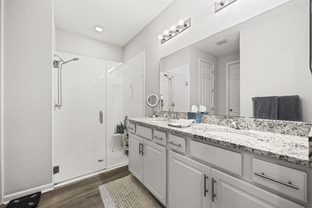 bathroom with wood finished floors, double vanity, a sink, and a stall shower