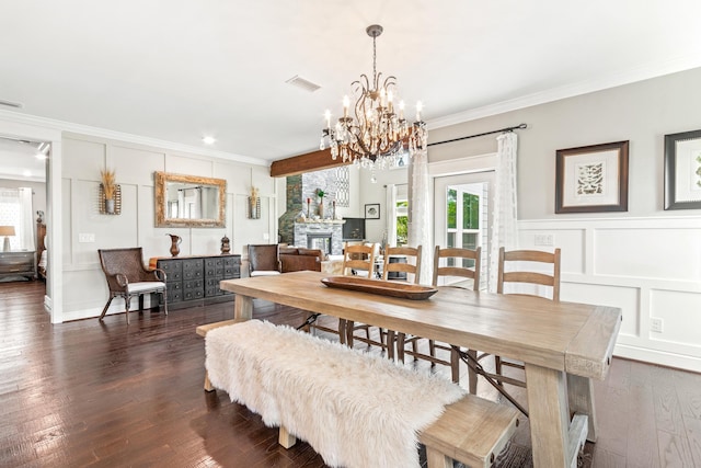 dining area featuring an inviting chandelier, dark wood-type flooring, a stone fireplace, and ornamental molding