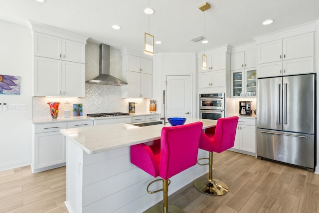 kitchen featuring white cabinetry, stainless steel appliances, light wood-style floors, wall chimney exhaust hood, and decorative backsplash