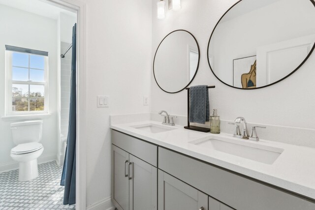 bathroom featuring double vanity, toilet, baseboards, and a sink