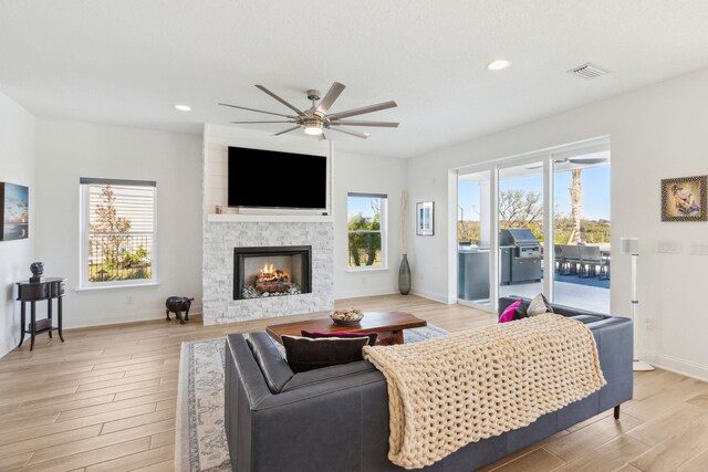 living room with visible vents, a stone fireplace, light wood finished floors, baseboards, and ceiling fan