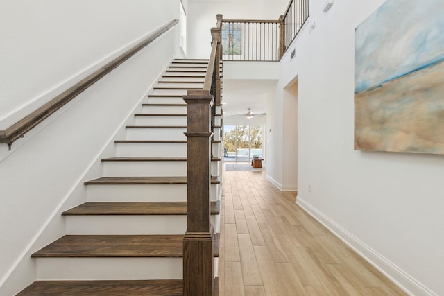 stairs featuring ceiling fan, baseboards, a high ceiling, and wood finished floors