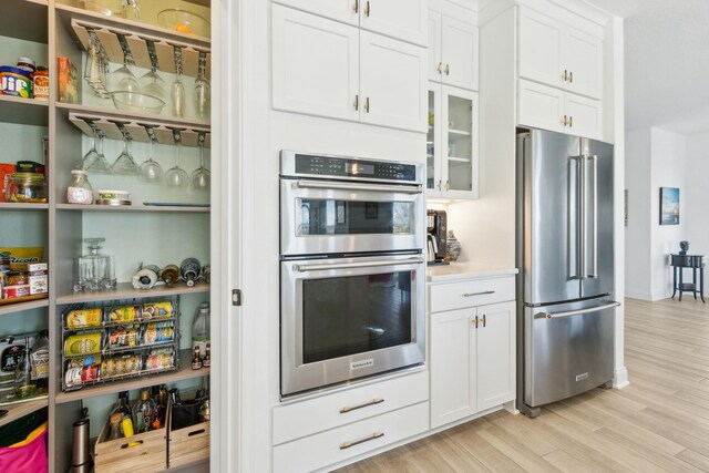 kitchen featuring glass insert cabinets, light wood-style floors, appliances with stainless steel finishes, and white cabinetry