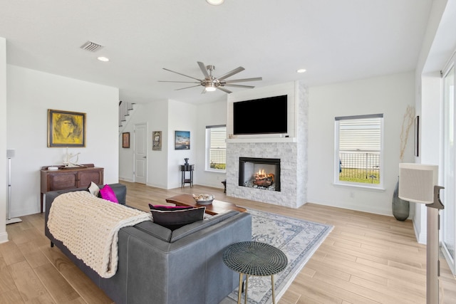 living area with a fireplace, visible vents, light wood finished floors, and a healthy amount of sunlight