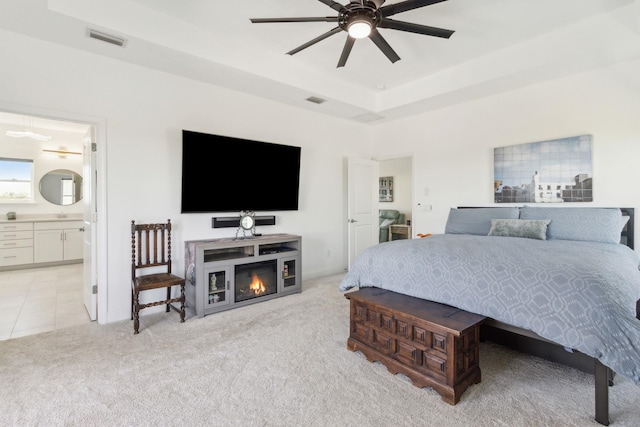 bedroom featuring visible vents, a raised ceiling, light colored carpet, and connected bathroom