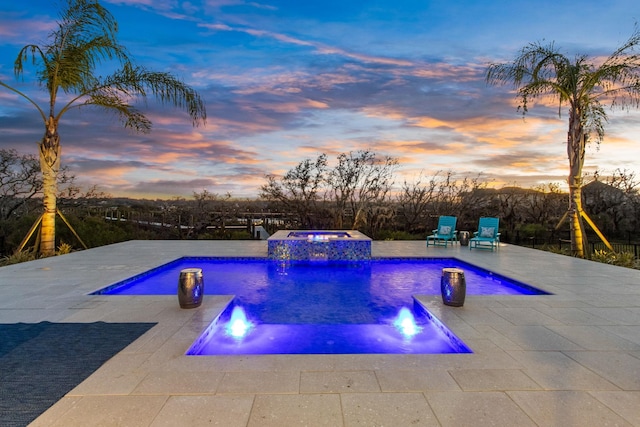 pool at dusk featuring a patio and a pool with connected hot tub