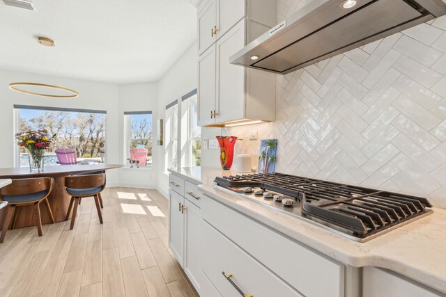 kitchen with decorative backsplash, white cabinets, under cabinet range hood, and stainless steel gas cooktop