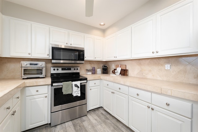 kitchen featuring white cabinets, light hardwood / wood-style floors, backsplash, and appliances with stainless steel finishes